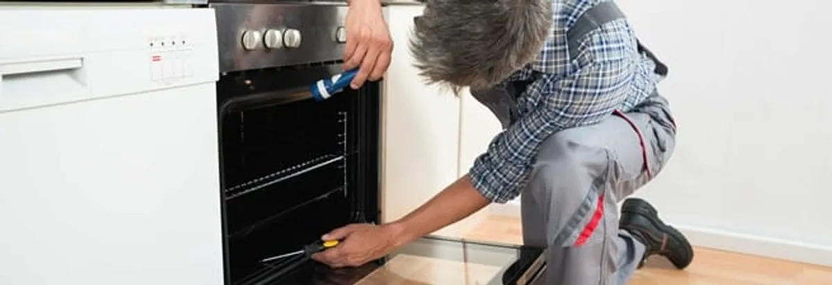 Oven repair technician inspecting and servicing an electric oven in Lowell, MA