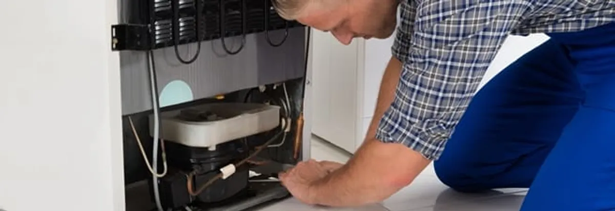Refrigerator repair technician servicing the compressor and condenser area in Lowell, MA