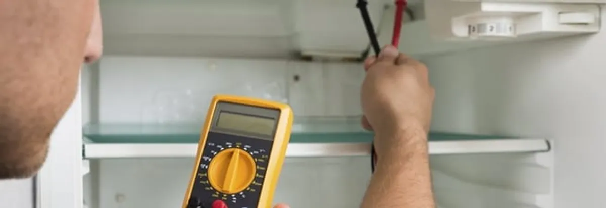 Refrigerator repair technician testing electrical components with a multimeter in Lowell, MA